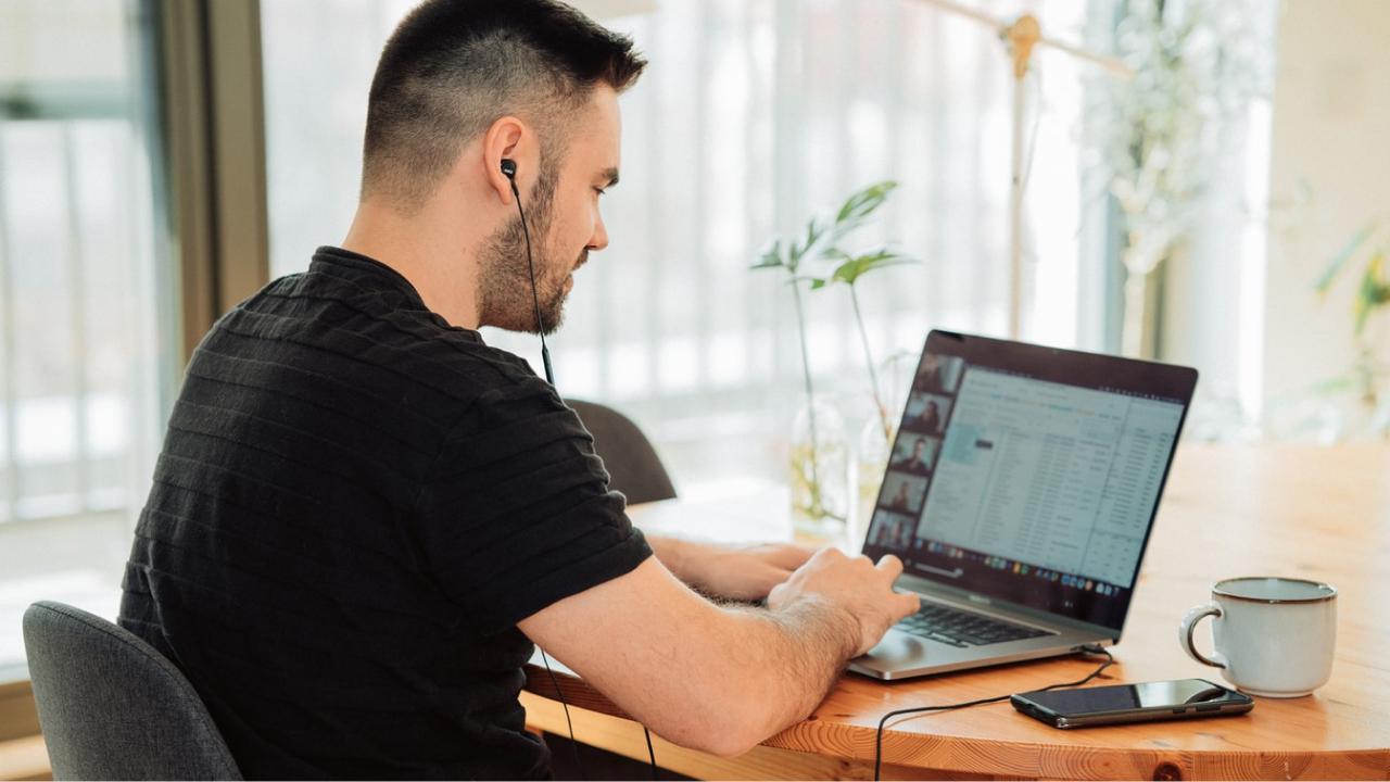 A person with their earphones in on a video call looking at their computer screen with coffee on the table